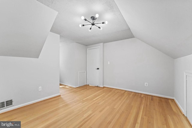 additional living space featuring vaulted ceiling, baseboards, a chandelier, visible vents, and wood finished floors