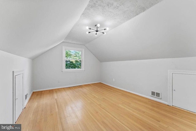 additional living space featuring lofted ceiling, baseboards, a textured ceiling, light wood-style floors, and visible vents