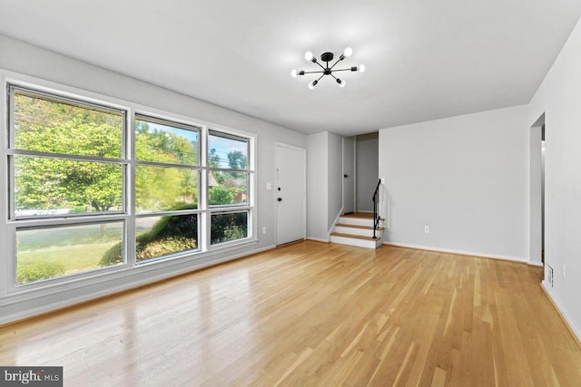 unfurnished living room featuring light wood-type flooring, a chandelier, and stairs