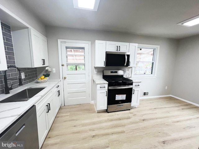 kitchen with light wood-type flooring, stainless steel appliances, decorative backsplash, a sink, and light stone countertops