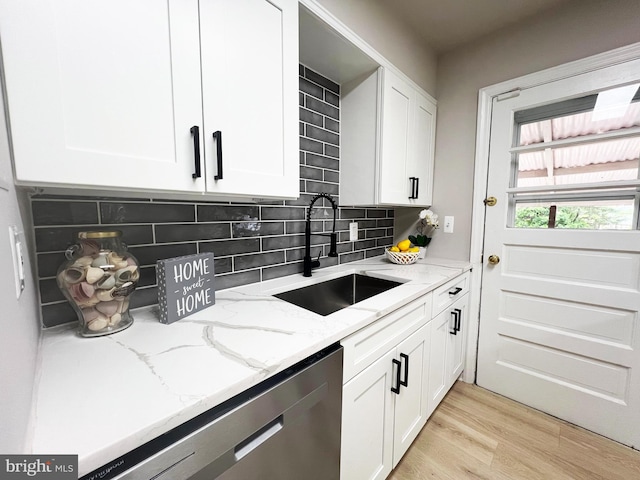 kitchen with light stone countertops, white cabinetry, a sink, light wood-style floors, and stainless steel dishwasher