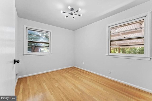 unfurnished room featuring an inviting chandelier, baseboards, light wood-style floors, and a wealth of natural light
