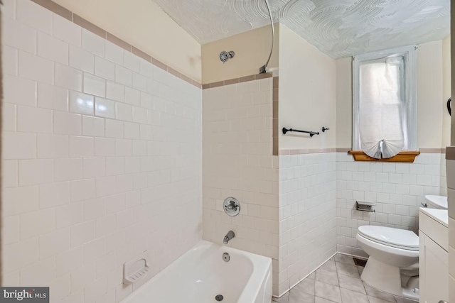 bathroom with tile walls, tub / shower combination, toilet, vanity, and tile patterned flooring