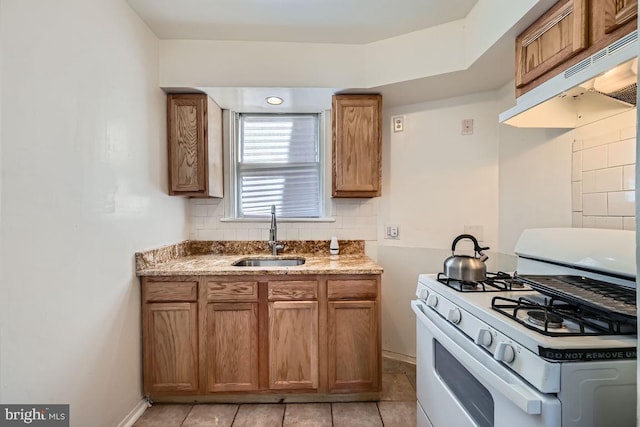 kitchen featuring a sink, white range with gas cooktop, brown cabinets, under cabinet range hood, and decorative backsplash