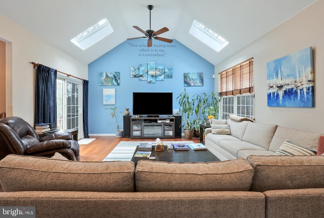 living room featuring vaulted ceiling with skylight, ceiling fan, baseboards, and wood finished floors