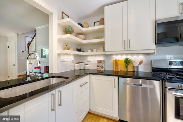 kitchen featuring white cabinets, appliances with stainless steel finishes, a sink, dark stone countertops, and backsplash