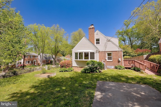 back of property featuring a wooden deck, a chimney, a yard, and brick siding