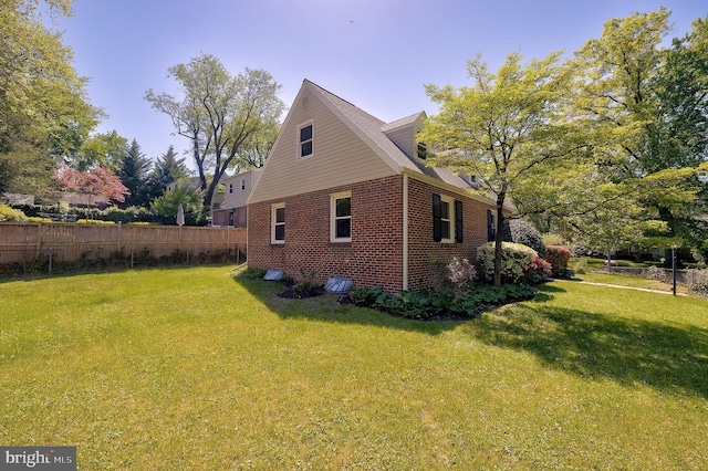 view of side of property featuring brick siding, a lawn, and fence