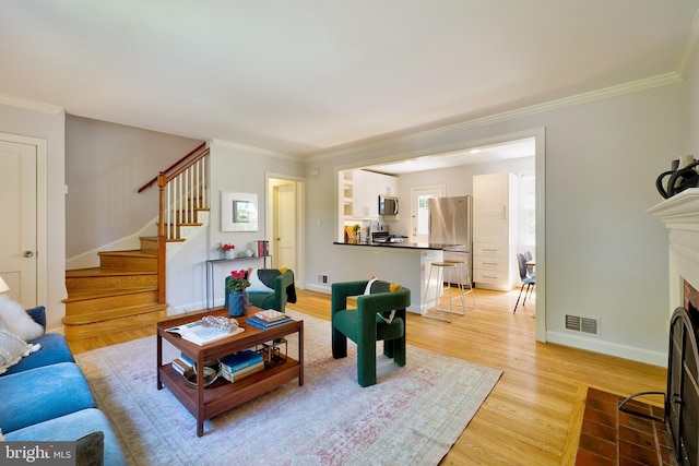 living area featuring visible vents, crown molding, stairs, a fireplace with flush hearth, and light wood-style flooring