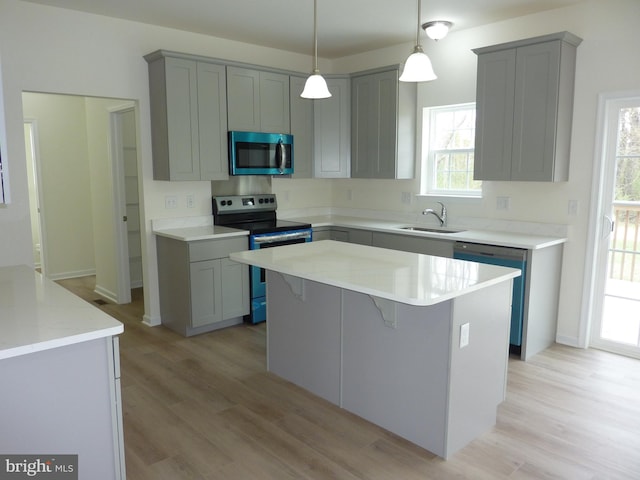 kitchen featuring light wood-style flooring, a kitchen island, gray cabinetry, stainless steel appliances, and a sink