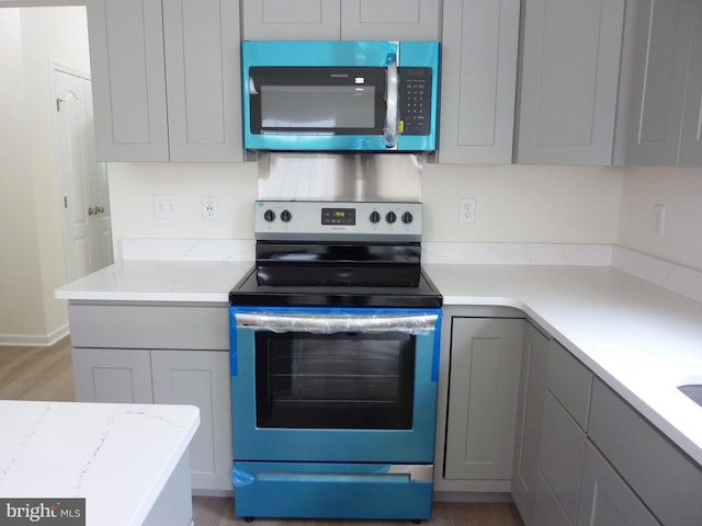 kitchen featuring light wood finished floors, gray cabinets, appliances with stainless steel finishes, and light stone countertops