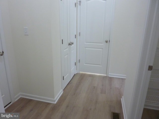 hall with light wood-style flooring, baseboards, and visible vents
