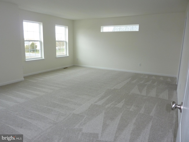 spare room featuring plenty of natural light, light colored carpet, and baseboards
