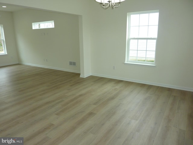 spare room with light wood-type flooring, a healthy amount of sunlight, a notable chandelier, and visible vents