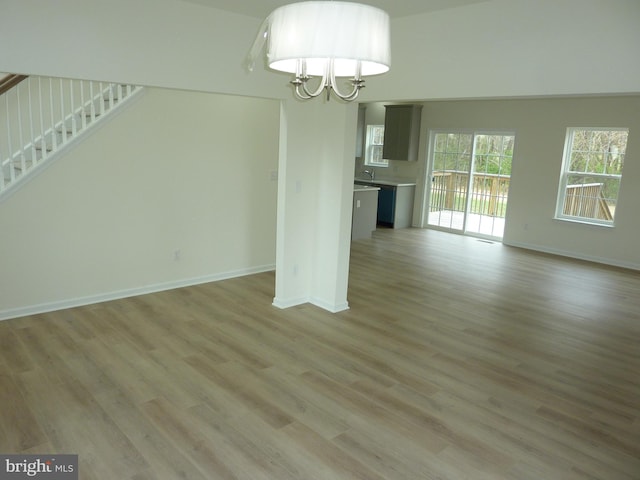 unfurnished living room featuring light wood finished floors, a notable chandelier, baseboards, and stairway