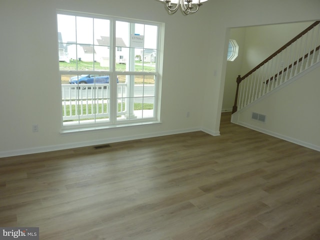 unfurnished living room with a notable chandelier, visible vents, baseboards, and wood finished floors
