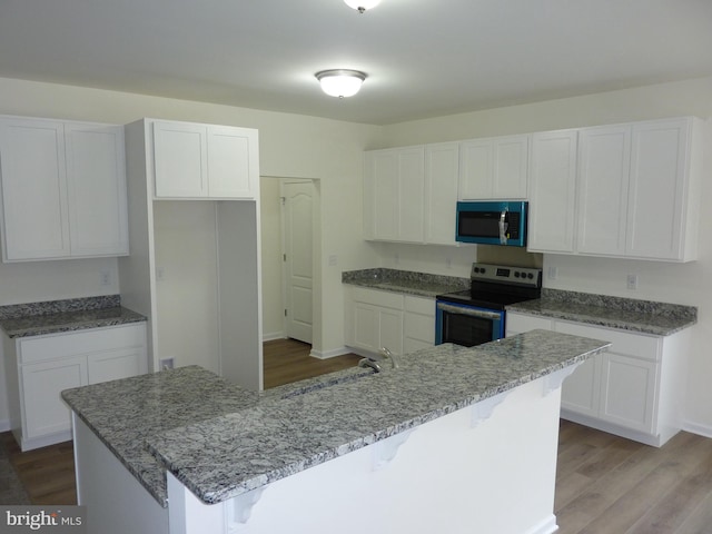 kitchen featuring wood finished floors, stainless steel range with electric stovetop, and white cabinets