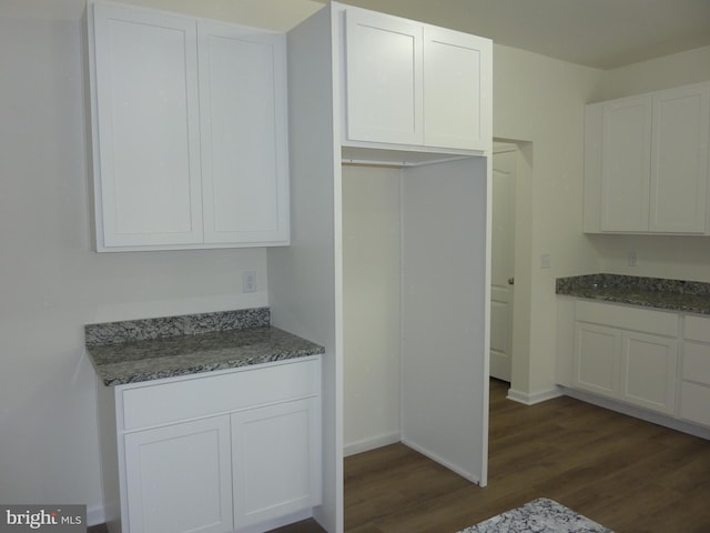 kitchen with dark wood-style flooring, white cabinets, dark stone countertops, and baseboards