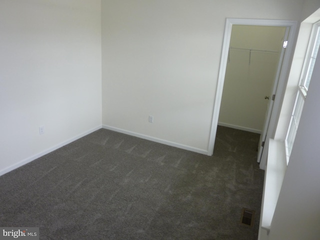 unfurnished bedroom with dark colored carpet, baseboards, a closet, a spacious closet, and visible vents
