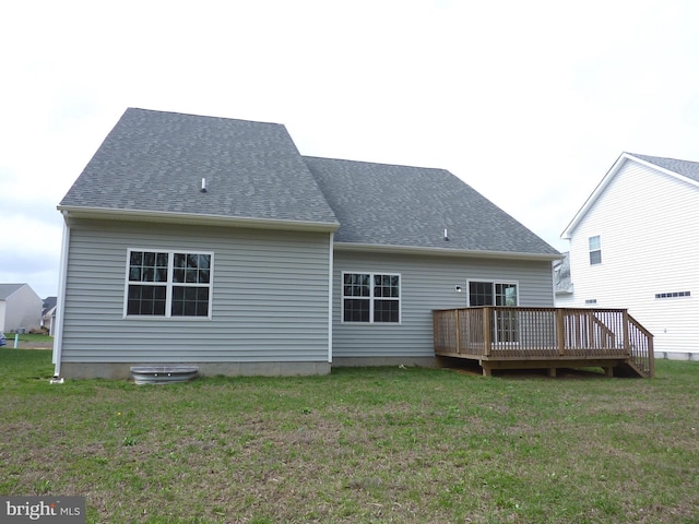 rear view of property featuring a shingled roof, a wooden deck, and a lawn