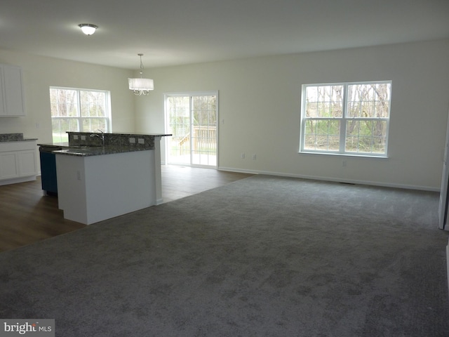 kitchen featuring dark colored carpet, a notable chandelier, white cabinetry, a kitchen island with sink, and pendant lighting