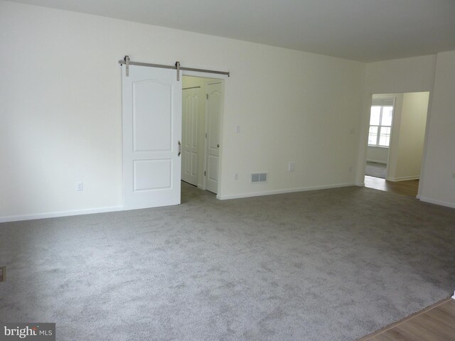 carpeted empty room featuring baseboards, visible vents, and a barn door