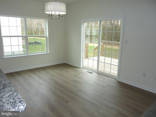 unfurnished dining area with visible vents, baseboards, an inviting chandelier, and wood finished floors