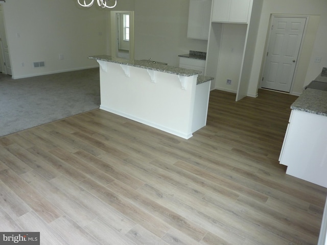 kitchen with visible vents, white cabinets, an inviting chandelier, a breakfast bar, and a kitchen island