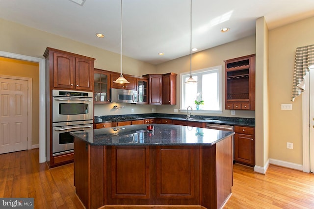 kitchen with glass insert cabinets, light wood-type flooring, a center island, appliances with stainless steel finishes, and a sink