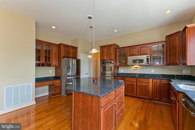 kitchen featuring built in desk, a center island, visible vents, stainless steel appliances, and wood finished floors