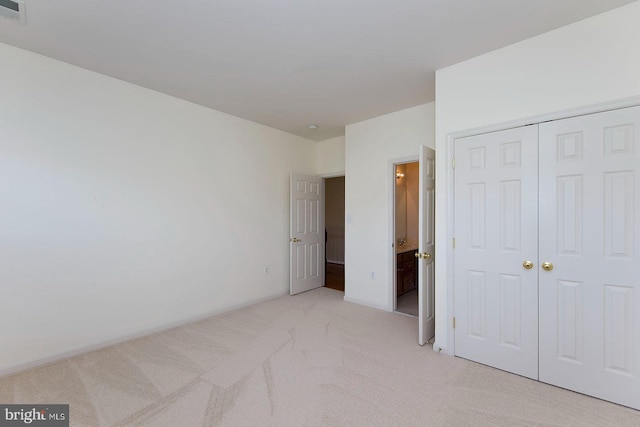 unfurnished bedroom featuring a closet, light colored carpet, and connected bathroom
