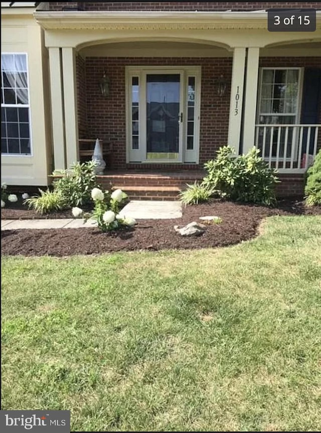 property entrance with a yard, covered porch, and brick siding