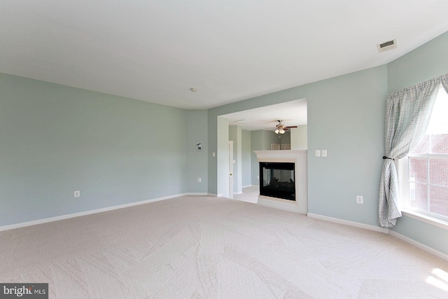 unfurnished living room featuring ceiling fan, a multi sided fireplace, light colored carpet, visible vents, and baseboards