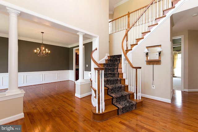stairs with wood finished floors, decorative columns, and ornamental molding