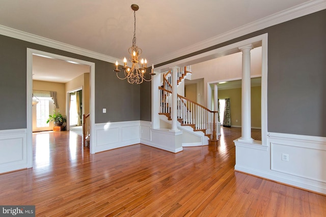 unfurnished dining area featuring a chandelier, crown molding, a wainscoted wall, stairs, and wood finished floors