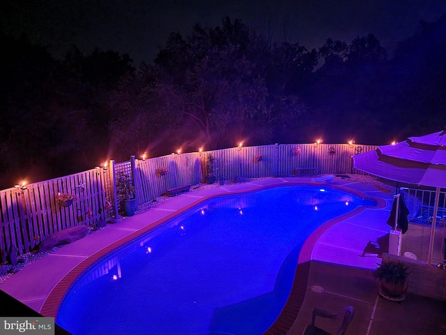 pool at night with a fenced backyard