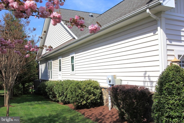 view of side of home featuring roof with shingles and a yard