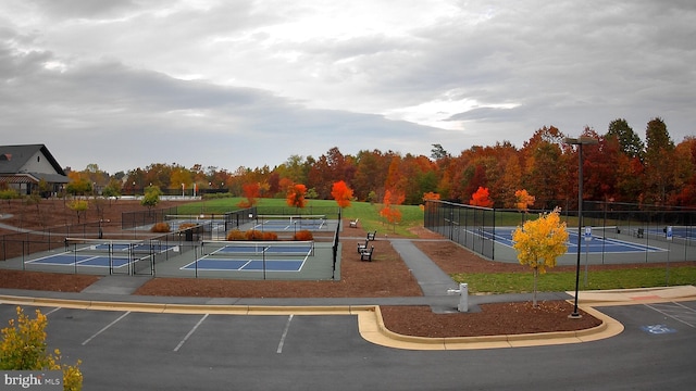 view of community with a tennis court, fence, and uncovered parking