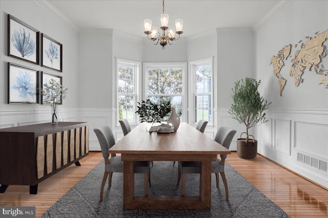 dining area with an inviting chandelier, ornamental molding, light wood-style flooring, wainscoting, and visible vents