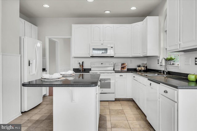 kitchen featuring a sink, dark countertops, white appliances, and white cabinetry