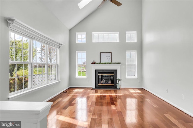 unfurnished living room featuring a glass covered fireplace, baseboards, a ceiling fan, and wood finished floors