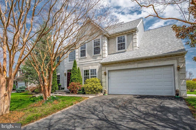 traditional home featuring an attached garage, driveway, and a shingled roof