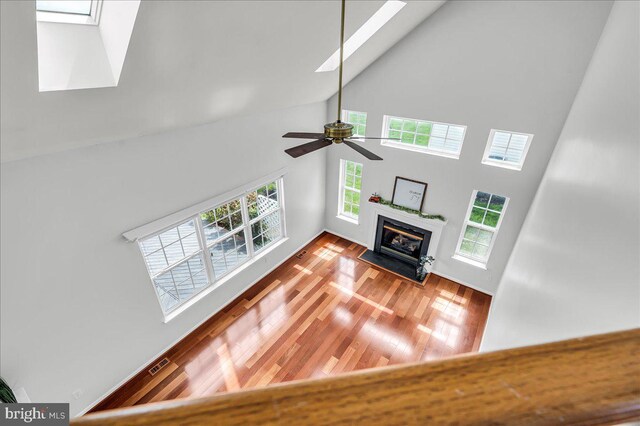 unfurnished living room featuring a fireplace with flush hearth, visible vents, a skylight, a high ceiling, and wood finished floors