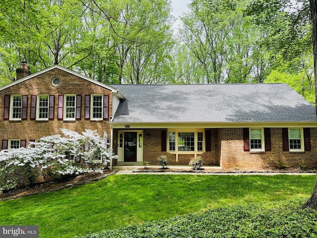 split level home featuring a shingled roof, a chimney, brick siding, and a front yard
