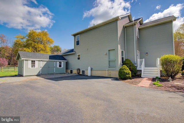 back of property with aphalt driveway, a storage shed, and an outdoor structure