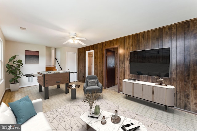 living room with wood walls, baseboards, ceiling fan, and visible vents