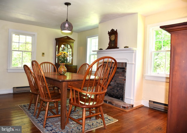 dining area with baseboards, a fireplace with raised hearth, a baseboard heating unit, and dark wood-style floors