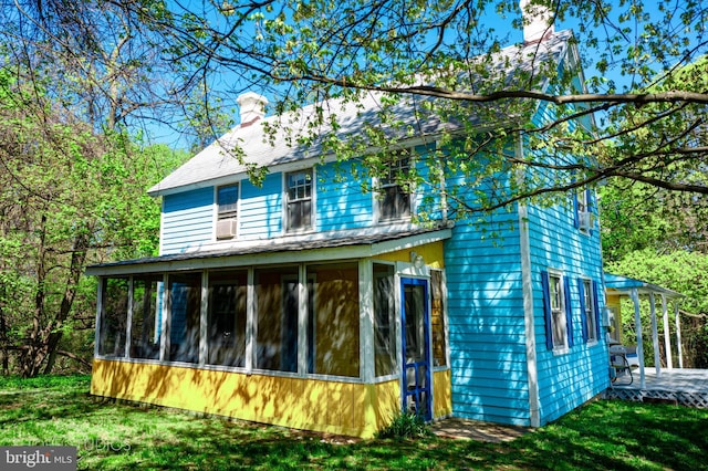 exterior space with a sunroom, a lawn, and a chimney