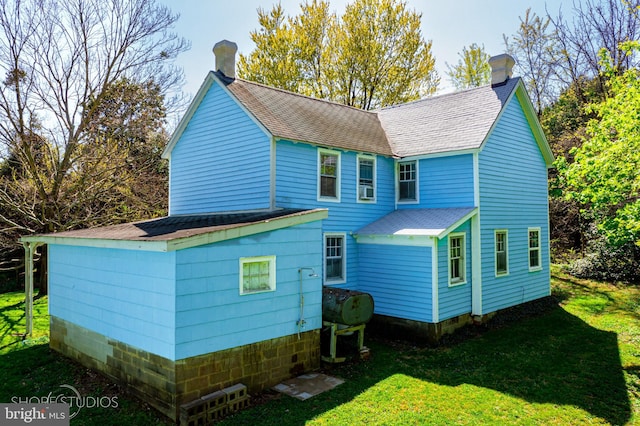 back of house with a lawn, a shingled roof, and a chimney