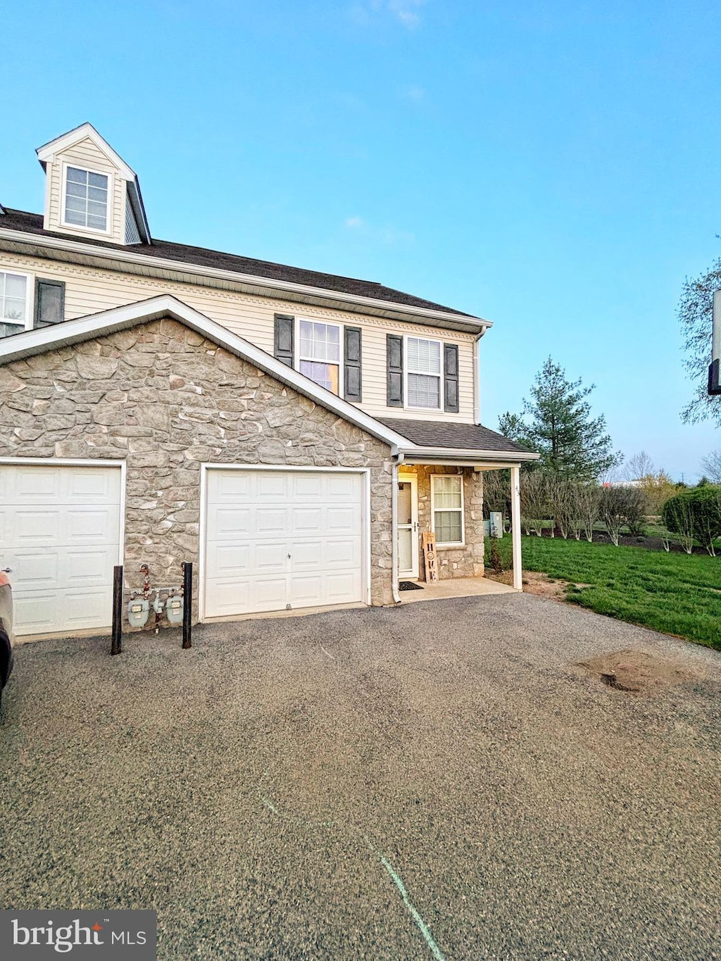 view of front of house featuring covered porch, a garage, driveway, and stone siding